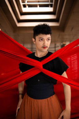 Asyalı bir adam gün içinde bedeni kırmızı bir bezle bağlandığı için ışığın altında duruyor.