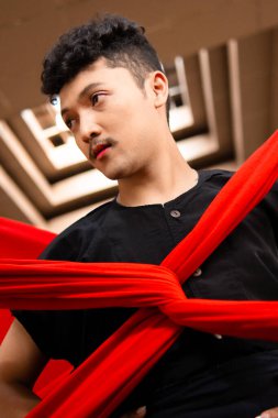 Asyalı bir adam gün içinde bedeni kırmızı bir bezle bağlandığı için ışığın altında duruyor.