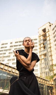 Asyalı bir adam gün boyu yüksek bir binanın önünde siyah bir kostüm içinde poz veriyor.