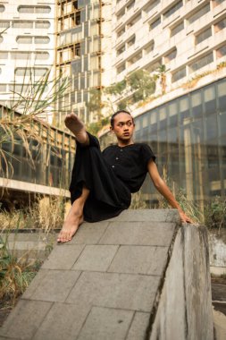 Asyalı bir adam eski bir binanın etrafında siyah elbiseler giyerken mermer bir kayanın üzerinde uyur.