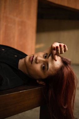 Kahverengi bir masada uyuyan Asyalı bir adam. Gün boyunca uzun saçları sarkmış.