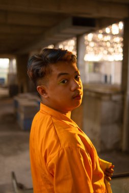 Terk edilmiş bir binanın penceresinin önünde duran Asyalı bir adam öğleden sonra sarı bir ceket giyiyordu.