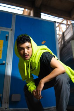 Siyah kıvırcık saçlı, yeşil kapüşonlu bir Asyalı.