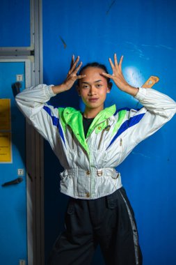 Eşcinsel bir Asyalı, gece molası sırasında mavi bir dolabın önünde eşofmanla poz veriyor.