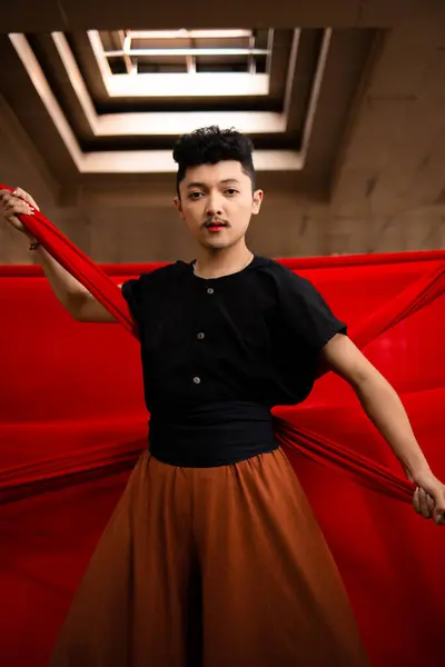 stock image an Asian man holding a red cloth in his arms with a bold expression against a red background during the day