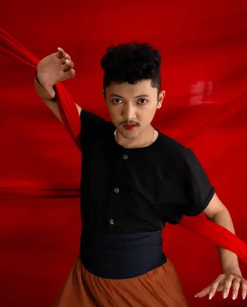 an Asian man holding a red cloth in his arms with a bold expression against a red background during the day