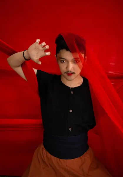 一个身穿黑色衬衫的亚洲男人 他的脸被一块红色的布遮住 在红色的背景面前有着可怕的面部表情 — 图库照片