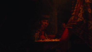 Bir şaman, gece bir masada büyü ve adak adama ayini yapıyor.