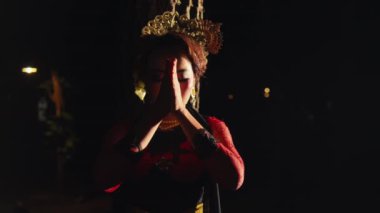 Asyalı bir kadın geceleri geleneksel bir Sundan kostümü giyerken ellerini kullanarak ritüel hareketleri yapıyor.