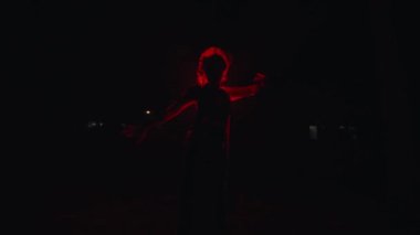 Asyalı bir kadın kırmızı ışığın önünde dans ediyor ve geceleri çok korkunç ve korkunç görünüyor.