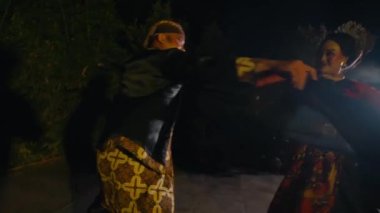 Ağaçlarla dolu çok canlı ve romantik bir sahnede dans eden bir çift ve geceleri sıcak ışıklar.