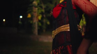 Asyalı bir kadın gece kırmızı bir kostüm giyerken çevik elleri ve siyah eşarpıyla dans ediyor.