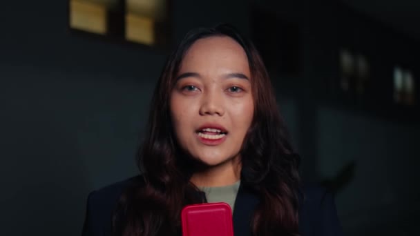 一位棕色头发和黑色外套的亚洲女人在晚上对着摄像机说话时就像个记者 — 图库视频影像