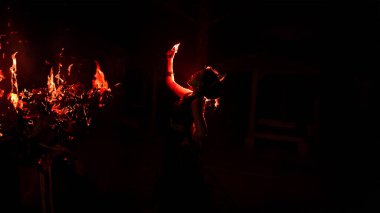 Hüzün dolu bir yüzle mücevherlerine bakan bir kadının silüeti ve geceleri etrafında yanan ateş.