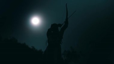 Siluetli bir kadın okçu gece yayını uçurumdan çekerken ayakta duruyor.