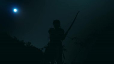 Siluetli bir kadın okçu gece yayını uçurumdan çekerken ayakta duruyor.