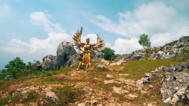 青い空に向かって岩山に立っている黄金の衣装と翼の女性の戦士 — ストック動画