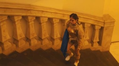 Altın zırhlı bir kadın şövalye savaş başlamadan önce kraliyet kolezyumunun merdivenlerinde ve koridorlarında yürüyor.