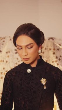 Orta boy bir portre resmi, hafifçe uzaklaşıyor. Zarif bir Cava kıyafeti giymiş biri dikkatlice aşağı bakar, sonra da doğrudan kameraya bakar..