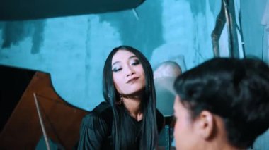 Oturan bir adamın perspektifinden omuz üstünden bir atış. Siyah gotik elbiseli bir kadın karanlık, mavi ışıklı, ürkütücü bir odada ona yaklaşıyor..