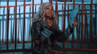 Alacakaranlıkta, metal parmaklıkların arkasında, perili evin içinde gizemli bir ambiyansı olan gümüş saçlı, gülümseyen kadın.