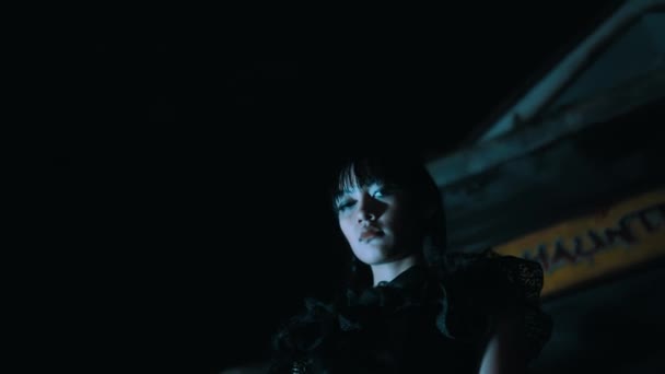 在漆黑的夜晚 穿着哥特式服装的恐怖女孩站在闹鬼的房子标志下 — 图库视频影像