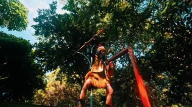 Kabile kıyafetli, kalkanlı, yemyeşil bir ormanda duran, gün ışığında eski savaşçı ruhunu anımsatan biri.
