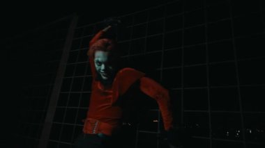 Kırmızı takım elbiseli ve palyaço makyajlı bir adam Cadılar Bayramı gecesi çok ürkütücü bir poz verirken gülüyor..