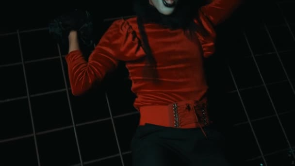 一个穿红衫 化着小丑妆的男人在铁栅栏前跳舞 摆出一副很恐怖的姿势 — 图库视频影像