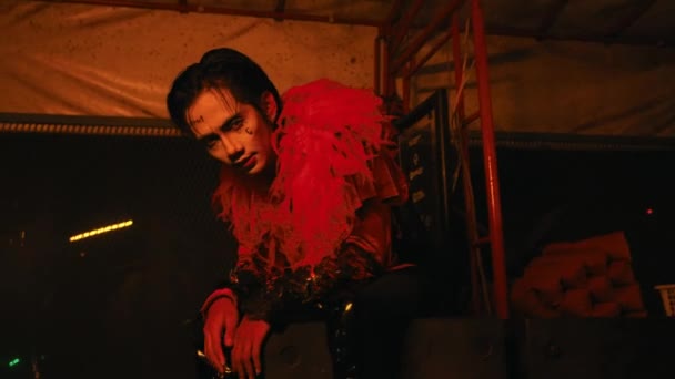 一个化着令人毛骨悚然的小丑模样的男人在一间夜间泛红的闹鬼的小屋里摆姿势 — 图库视频影像