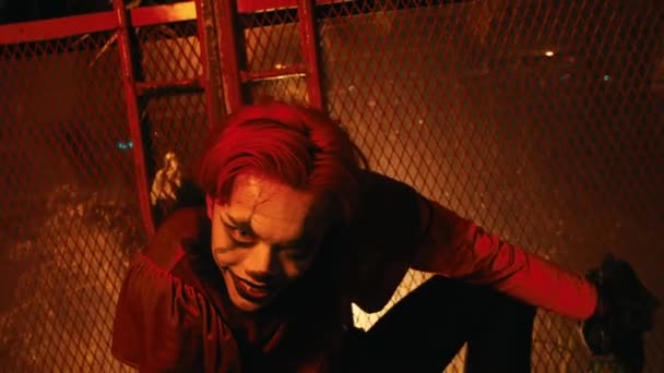 一个毛茸茸的小丑 留着红头发 穿着红衣 在一个晚上点着红光的闹鬼的小屋里摆姿势跳舞 — 图库视频影像