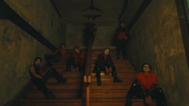 Bir grup insan loş bir merdivende oturmuş, gece boyunca karamsar ve düşünceli bir atmosfer yayıyorlar.