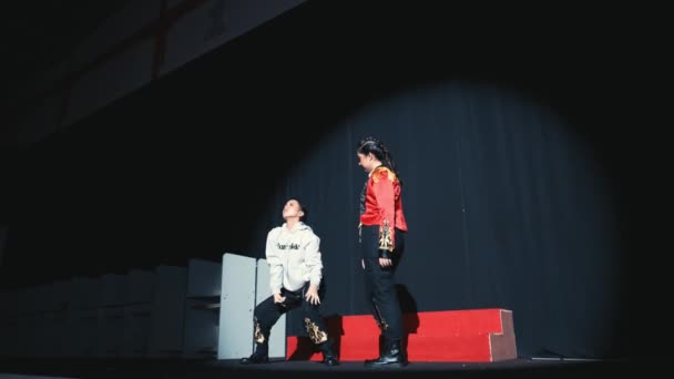 两名表演者 一个身穿白色服装 另一个穿着红色夹克 穿着戏剧化的灯光 在舞台上表演 传达着夜晚的动感和娱乐感 — 图库视频影像