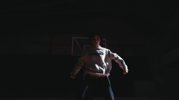 在黑暗的体育馆里 一个篮球运动员的轮廓 在黑暗的体育馆里 他准备在篮筐下行动 晚上还带着戏剧性的灯光 — 图库视频影像