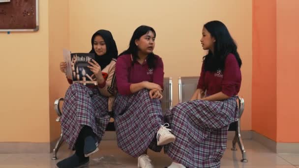 学校の制服を着た3人の若い女性が屋内で座ってしゃべり ある女性が朝に雑誌を読んでいた — ストック動画