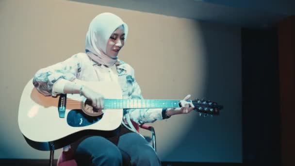 Mulher Sorridente Hijab Tocando Guitarra Acústica Enquanto Sentada Uma Cadeira — Vídeo de Stock