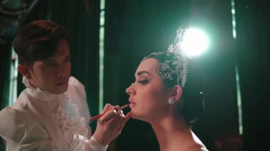 Makyaj sanatçısı, gece boyunca sahne arkasında zarif başlıklı bir modele ruj sürüyor.