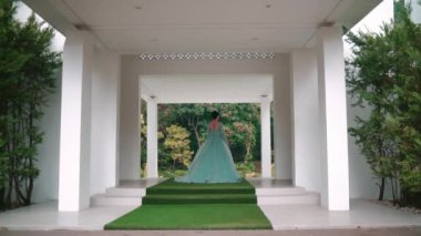 Gündüz vakti bahçe manzaralı modern bir binanın girişinde duran zarif elbiseli kadın.