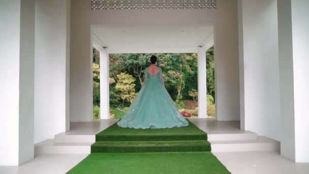 清晨时分 身穿飘逸的绿色长裙的优雅女子站在一座俯瞰花园的现代白色亭子门口 — 图库视频影像