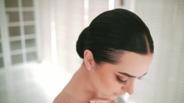 Pencere kenarında çörek saç stili, yumuşak ışık, gün ışığında profil manzaralı zarif bir kadın.