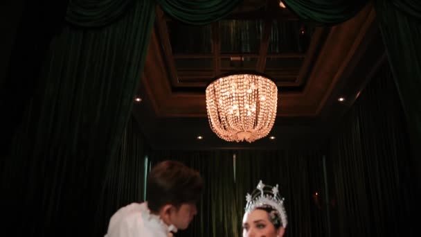 身穿闪亮连衣裙头冠的优雅女人坐在吊灯下 晚上由一名造型师化妆 — 图库视频影像