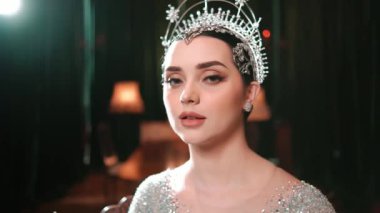 Ön tarafta, gümüş tacıyla kraliçe gibi giyinmiş çarpıcı bir kadının portresi var. Kusursuz göz kamaştırıcı makyajla kendinden emin görünüyor. Son moda konsepti.