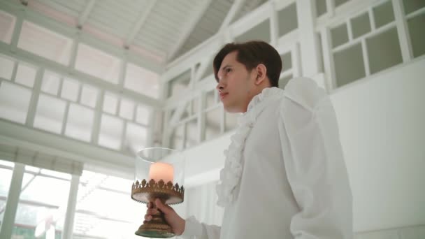 身穿白衣的文静男子拿着一支点燃的蜡烛 在一间有大窗的宁静的房间里 — 图库视频影像