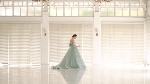 明るく空気のある部屋を歩き回る流れるドレスのエレガントな女性 大きな窓と朝のシャンデリア — ストック動画