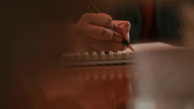 Bir insanın ellerinin, sabah bulanık bir ön planı olan ahşap bir masanın üzerine yazılmış bir deftere yakın plan fotoğrafı.