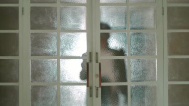 Buzlu cam kapıların arkasında duran bir insanın silueti gün ışığında gizem ve mahremiyet hissi yaratıyor.
