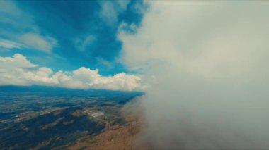 Açık mavi gökyüzü ve kabarık bulutlarla kaplı hava manzarası, gün ışığında kara ve gökyüzü arasındaki zıtlığı betimliyor.