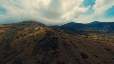 Gün ışığında dramatik bulutlu bir gökyüzü altında engebeli bir dağ manzarası.