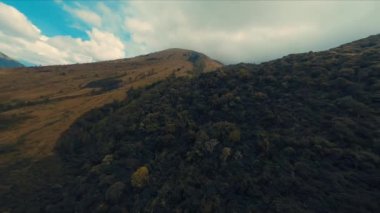 Gündüz vakti bulutlu bir gökyüzü altında yemyeşil, uçsuz bucaksız, yuvarlanan bir manzaranın havadan görüntüsü.