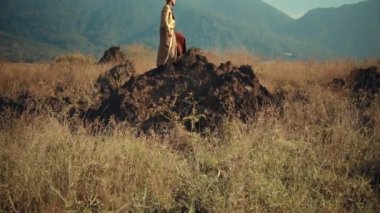 Geleneksel altın rengi bir Cava kostümü giyen bir adam kayalık bir çıkıntıda durup arkasında bir dağ sırasıyla uzaklığa bakar..
